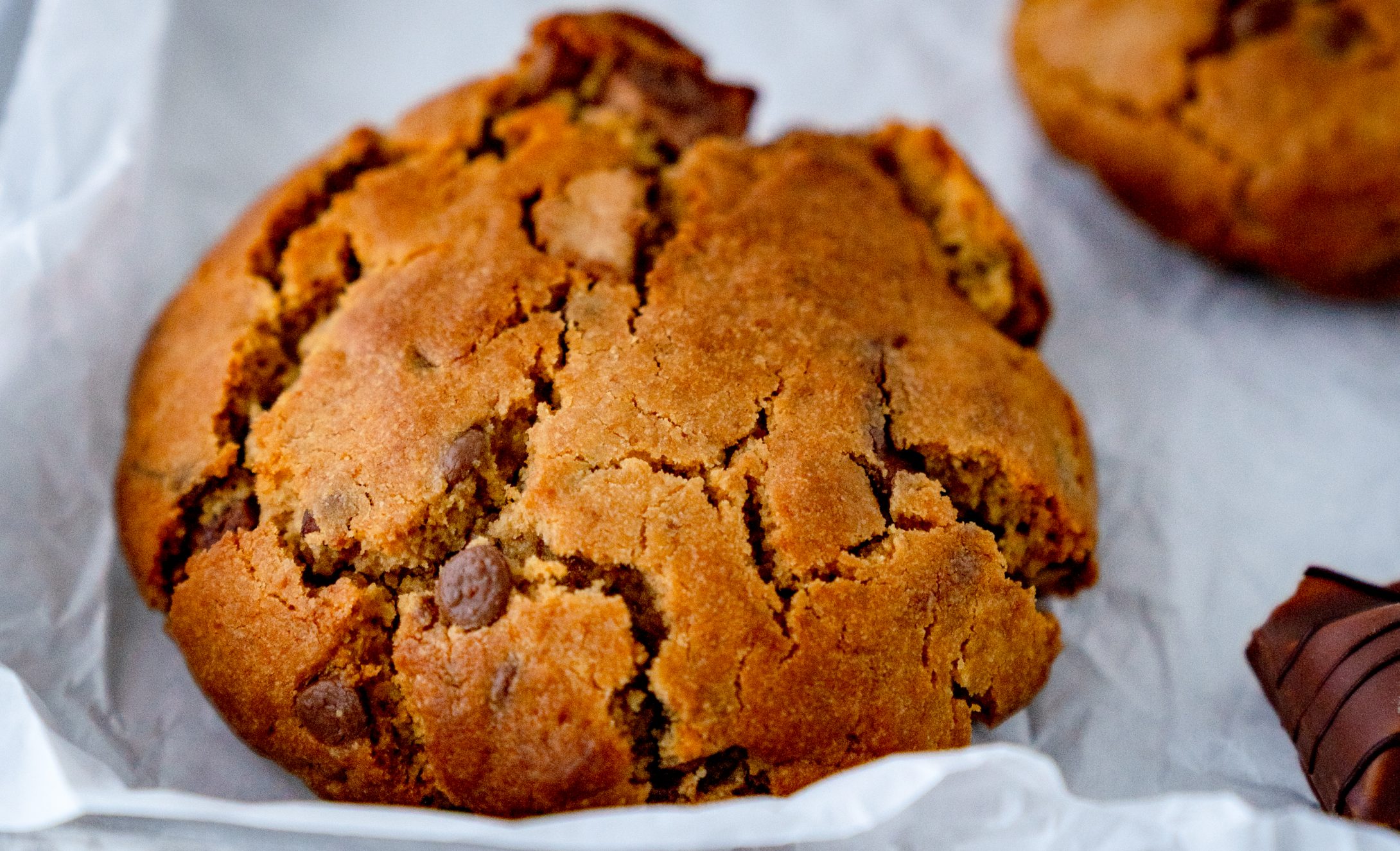 Ein Nutella Cookie aus der Heißluftfritteuse und ein weiterer Cookie, soweie Schokoriegel im Anschnitt auf einem weißen Backpapier
