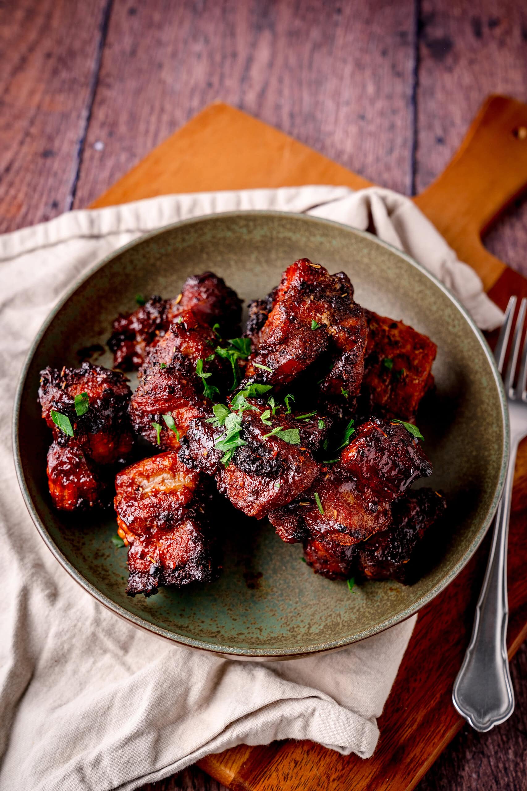 Saftige Pork Belly Burnt Ends aus der Heißluftfritteuse in dunkler BBQ-Sauce auf einem Teller und Holzbrett