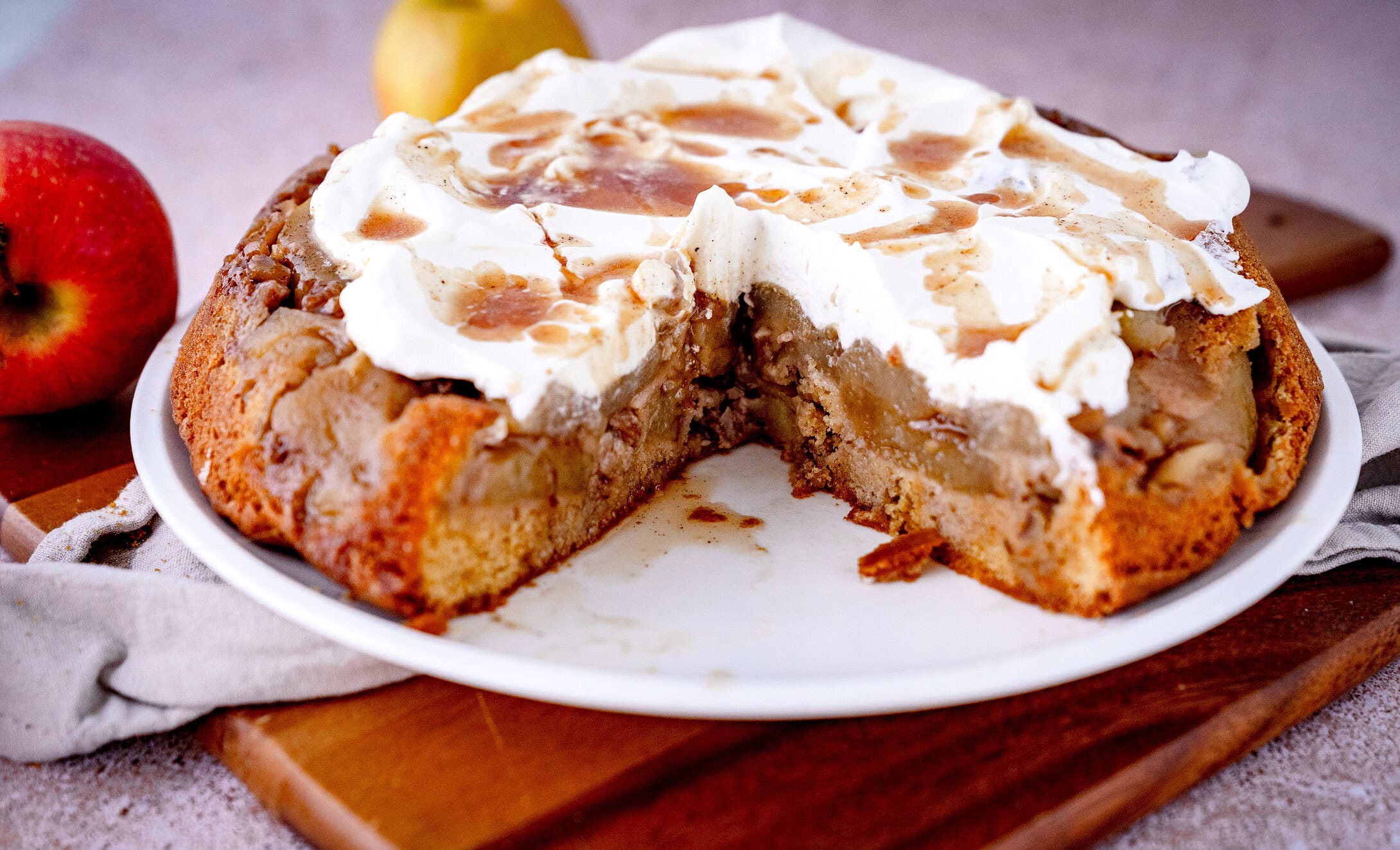 Gestürzter Apfelkuchen mit Walnüssen und Sahne sowie Gewürzsud auf weißem Teller mit Äpfeln