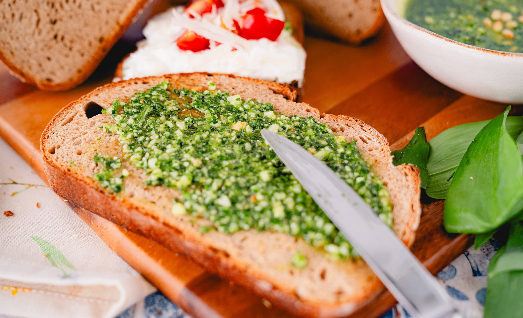 Bärlauchpesto, das mit Pinienkernen und Parmesan auf eine Brotscheibe gestrichen wird