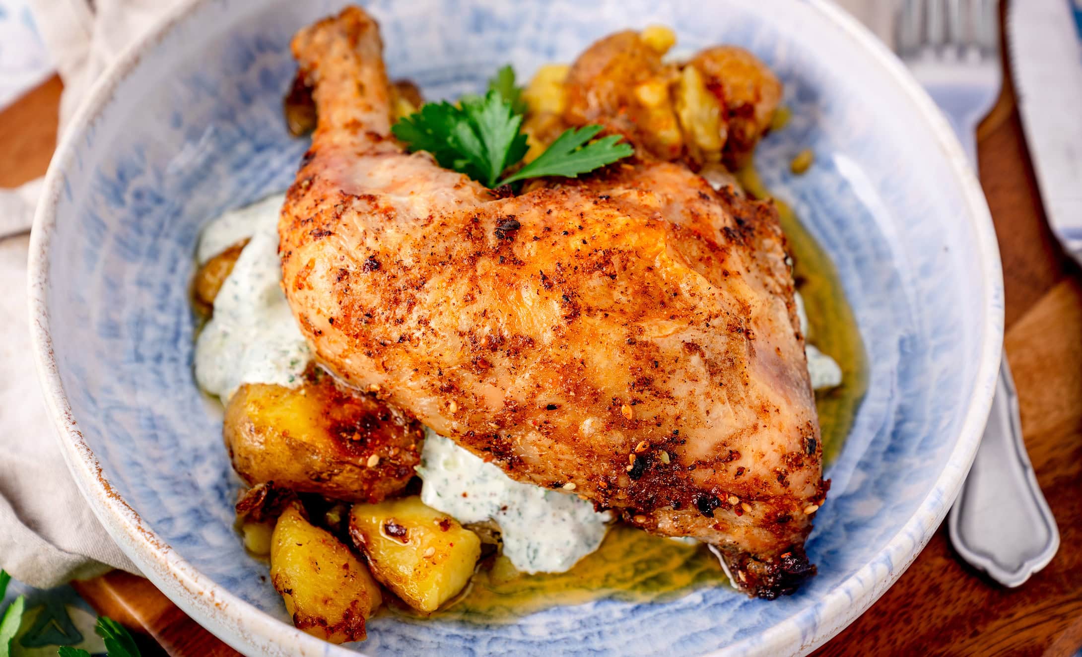 Nahaufnahme eines Za'atar Hähnchenschenkels auf einem blauen tiefen Teller mit Kartoffeln und einem Joghurtdip
