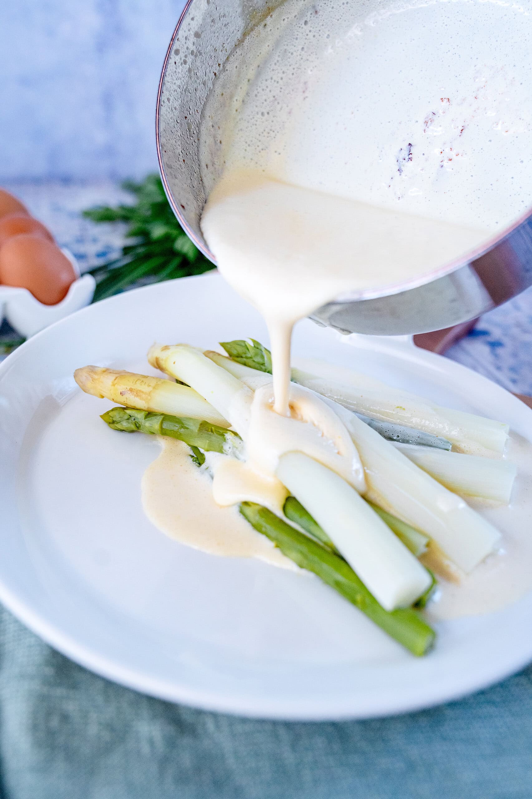 Blitz-Hollandaise, die über grünen und weißen Spargel gegossen wird